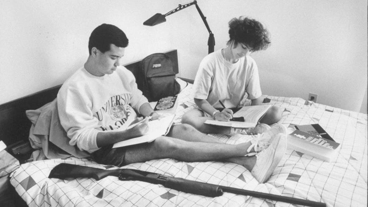 Justin Walker and Christine Smith sit on a bed with books and a shotgun for protection in an apartment.