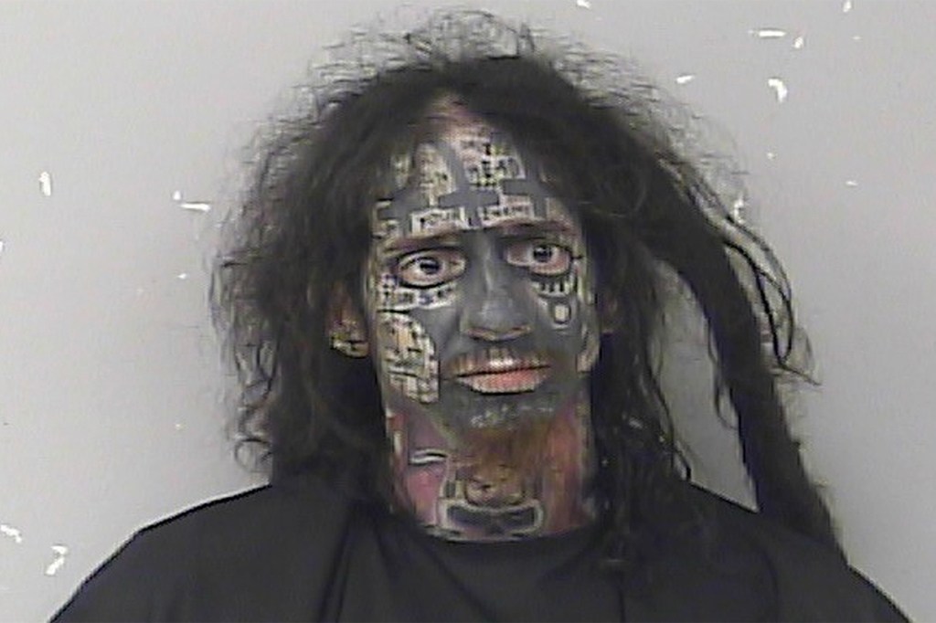 Mark Stephen Asea in a mugshot with extensive facial tattoos and long, dark hair.