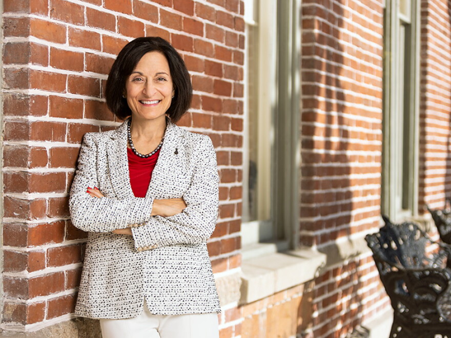 Woman with short brown hair with her arms crossed and leaning against a brick building