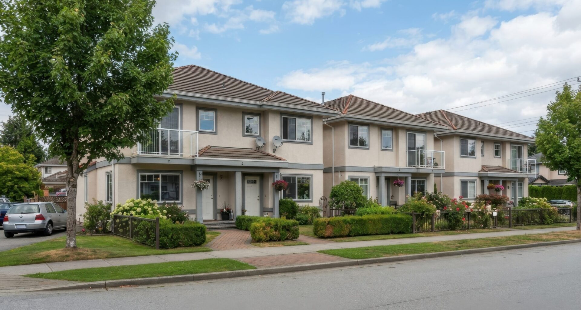 Two-story townhomes with balconies, landscaped front yards and a sidewalk along a residential street.