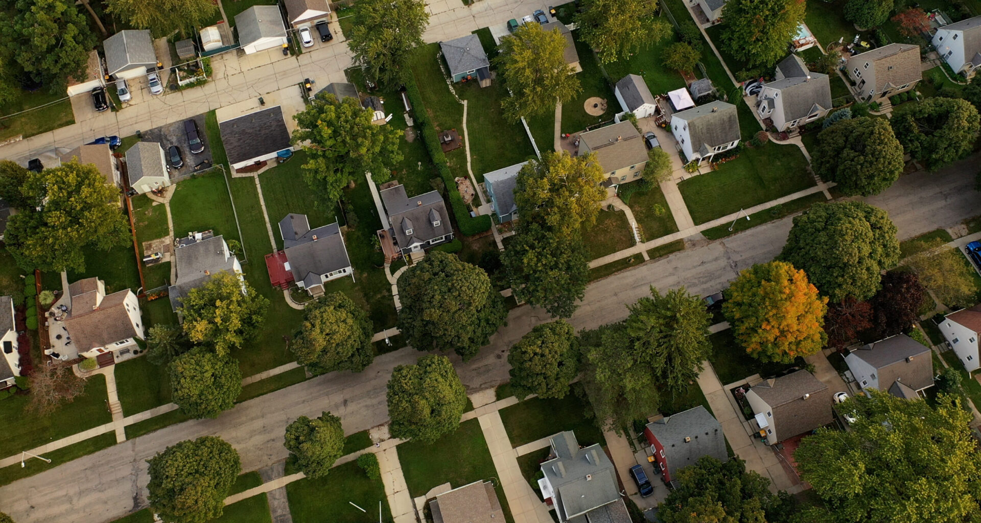 Aerial view of a residential neighborhood with single-family homes, tree-lined streets, driveways and lawns.
