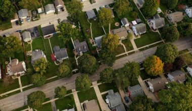 Aerial view of a residential neighborhood with single-family homes, tree-lined streets, driveways and lawns.