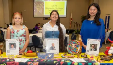 Three students stand with displays noting their winning essays in a Hispanic Heritage Month contest.
