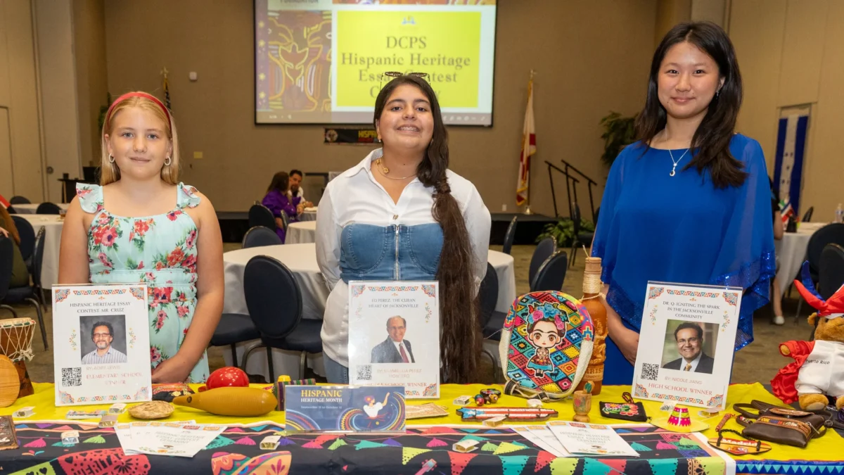 Three students stand with displays noting their winning essays in a Hispanic Heritage Month contest.