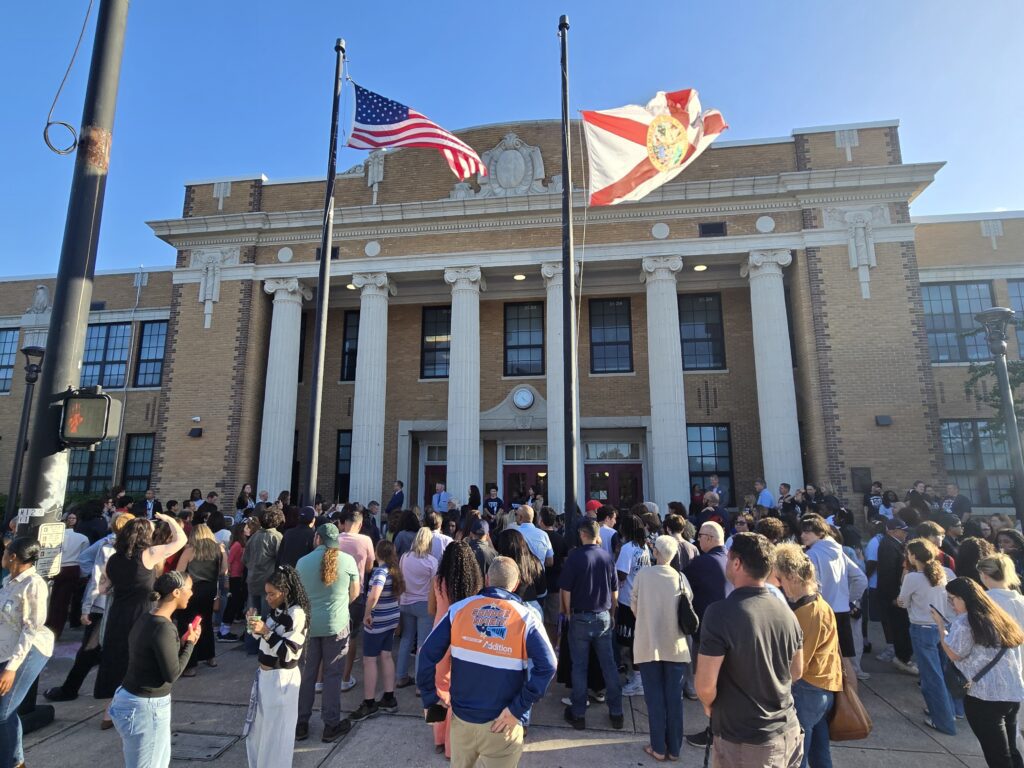 a group of people standing out from of an old, colonnaded school.