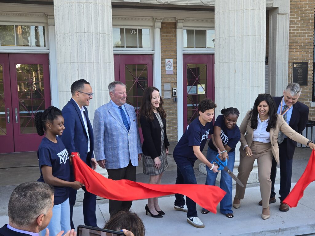 Dignitaries cutting a ribbon in front of a school