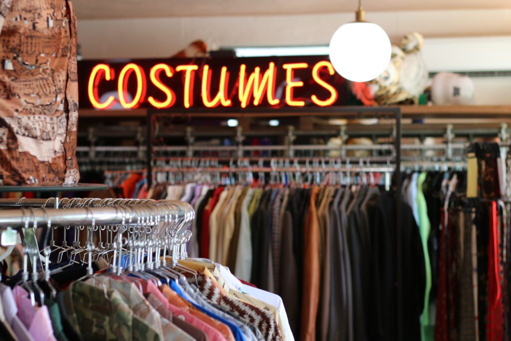 neon sign says COSTUMES above clothing racks