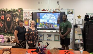 From left to right: GFWC Apopka Woman's Club President Diane Harrison, Clay Springs Elementary School Partners in Education Coordinator Christine Muchow, and Clay Springs P.E. coach Aden Jackson pose with a picture of Minto Primary School students receiving the equipment.