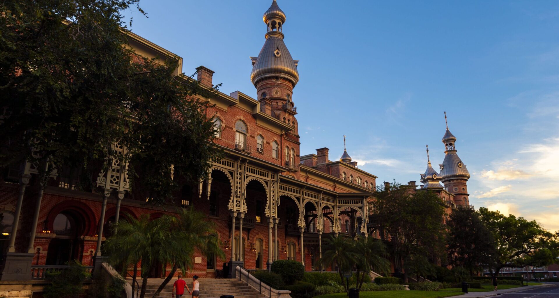 Historic Plant Hall at the University of Tampa, featuring red brick architecture, ornate verandas and distinctive silver minarets at sunset.