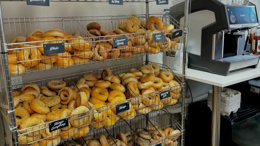 array of bagels arranged behind a counter. The bagels are organized in wire baskets