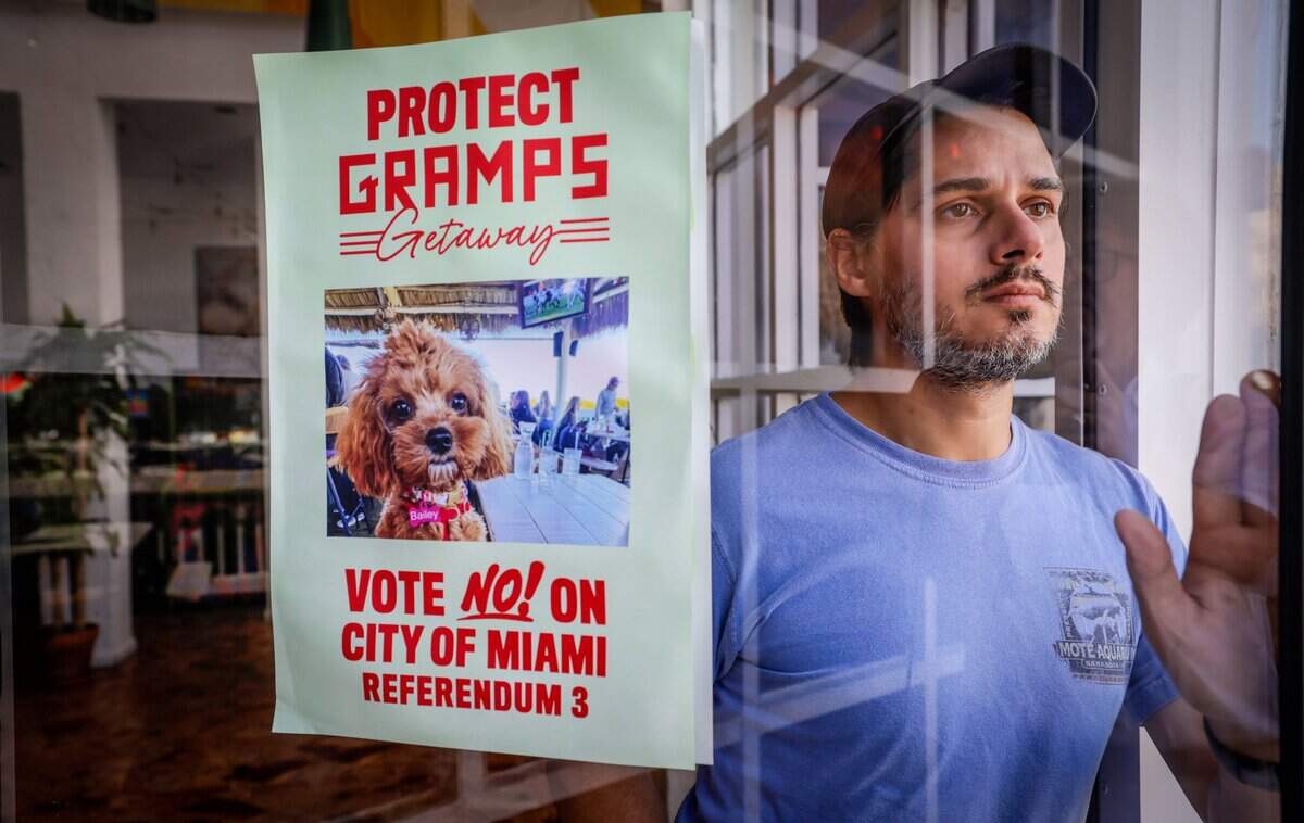 Justin Mendoza Routt, a senior advisor to Adam Gersten, owner of Gramps Getaway, stands at a doorway at Gramps Getaway restaurant with a poster urging Miami voters to vote no on City of Miami referendum 3, which will be on the November ballot. Gramps Getaway sits along the Rickenbacker Causeway in Miami, Florida, on Tuesday, October 6, 2026. Miami voters will decide whether to lease about 27.6 acres of publicly owned waterfront on Virginia Key to a private developer for up to 75 years.