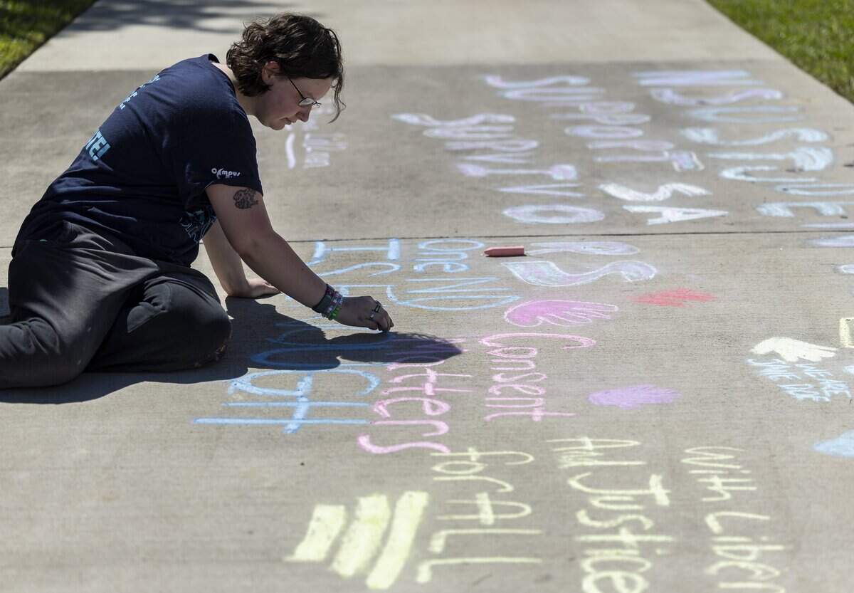 Psychology student Madelynn Parrish, 18, writes messages during a protest in front of the Alvin Sherman Library at Nova Southeastern University on Thursday, Oct. 15, 2026, in Davie, Fla. Students are protesting the university's handling of allegations involving a former Cornell University student who is accused in a sexual assault lawsuit.