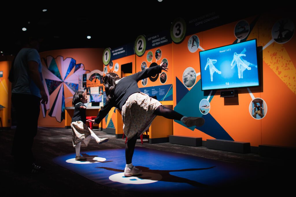 Two children balance on one foot in front of a screen at the Orlando Science Center's new exhibit.