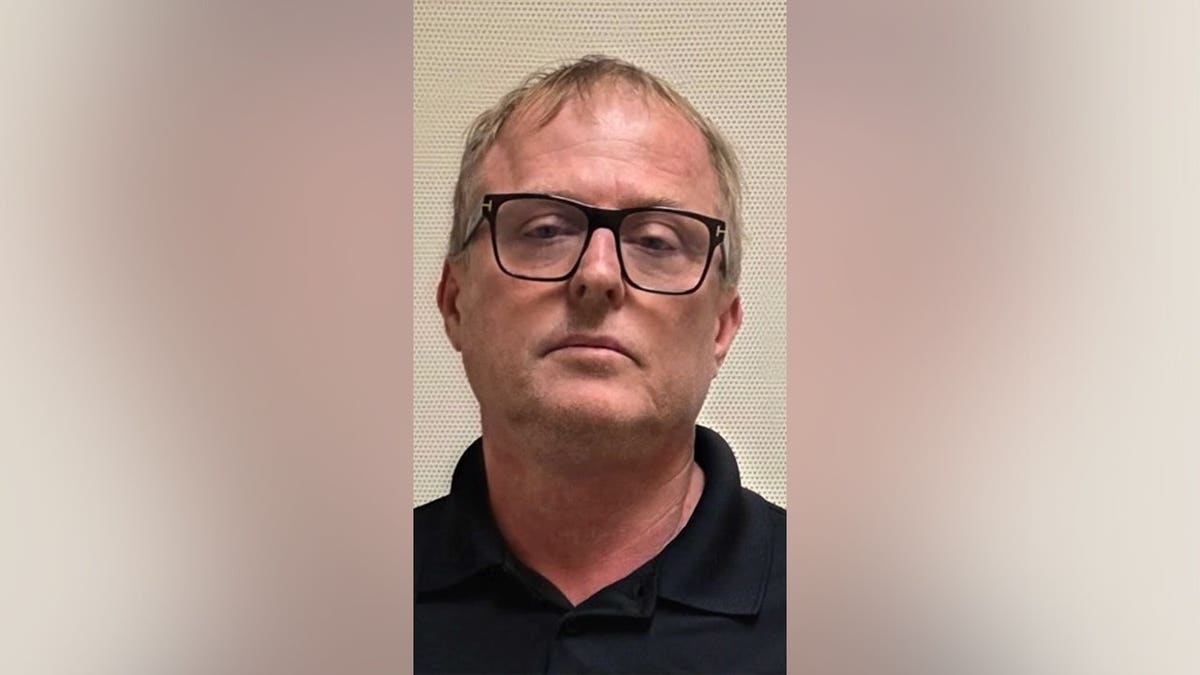 Close-up booking photo of Dale Smith Jr. wearing black-framed glasses and a black collared shirt against a light-colored background.