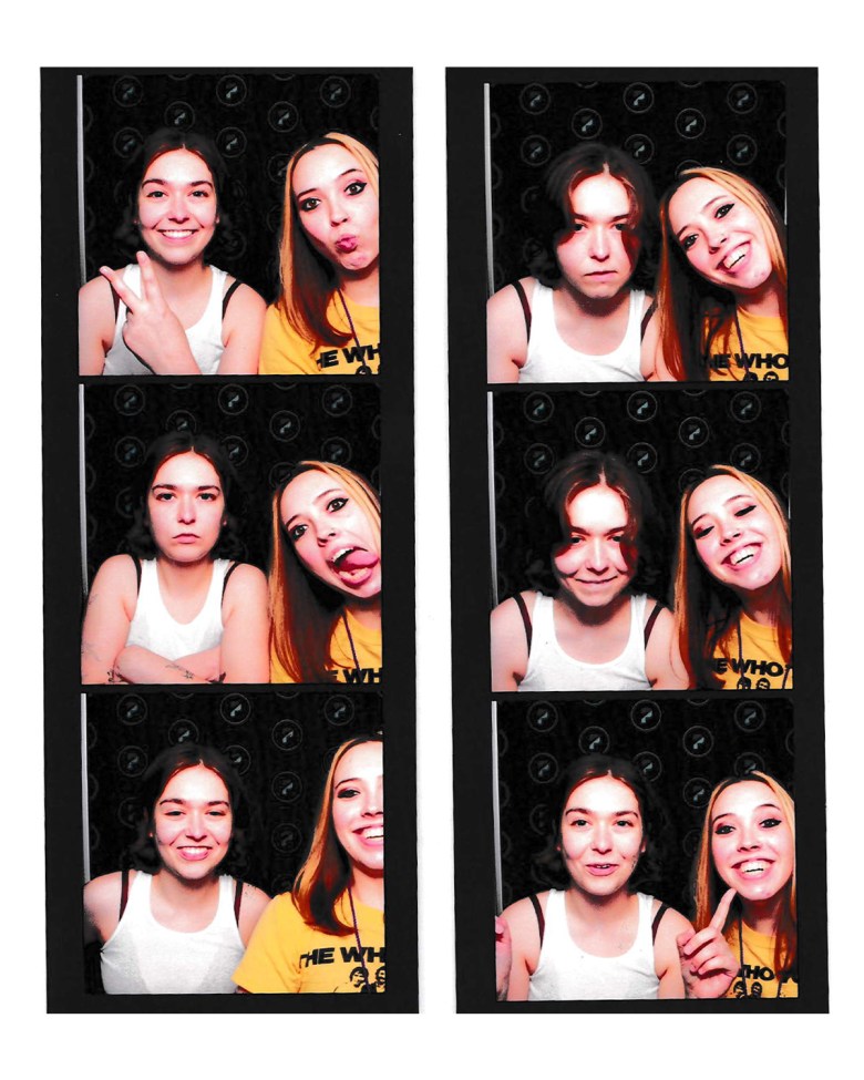 A six-frame photo booth strip showing (L-R) Snail Mail's Lindsey Jordan and Sophie Allison of Soccer Mommy. Displayed across two vertical strips of three photos each set against a white border and black background, Lindsey Jordan (left) wears a white tank top with dark hair, while Sophie Allison (right) wears a yellow shirt featuring "THE WHO" text. The pair strikes various playful poses—including peace signs, wink expressions, crossed arms, and wide smiles—under sharp photo booth flash lighting.