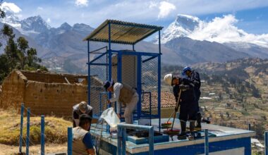 Workers maintain a water facility in a mountainous rural community, with snow-capped peaks in the background.