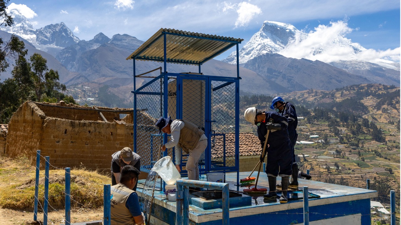 Workers maintain a water facility in a mountainous rural community, with snow-capped peaks in the background.