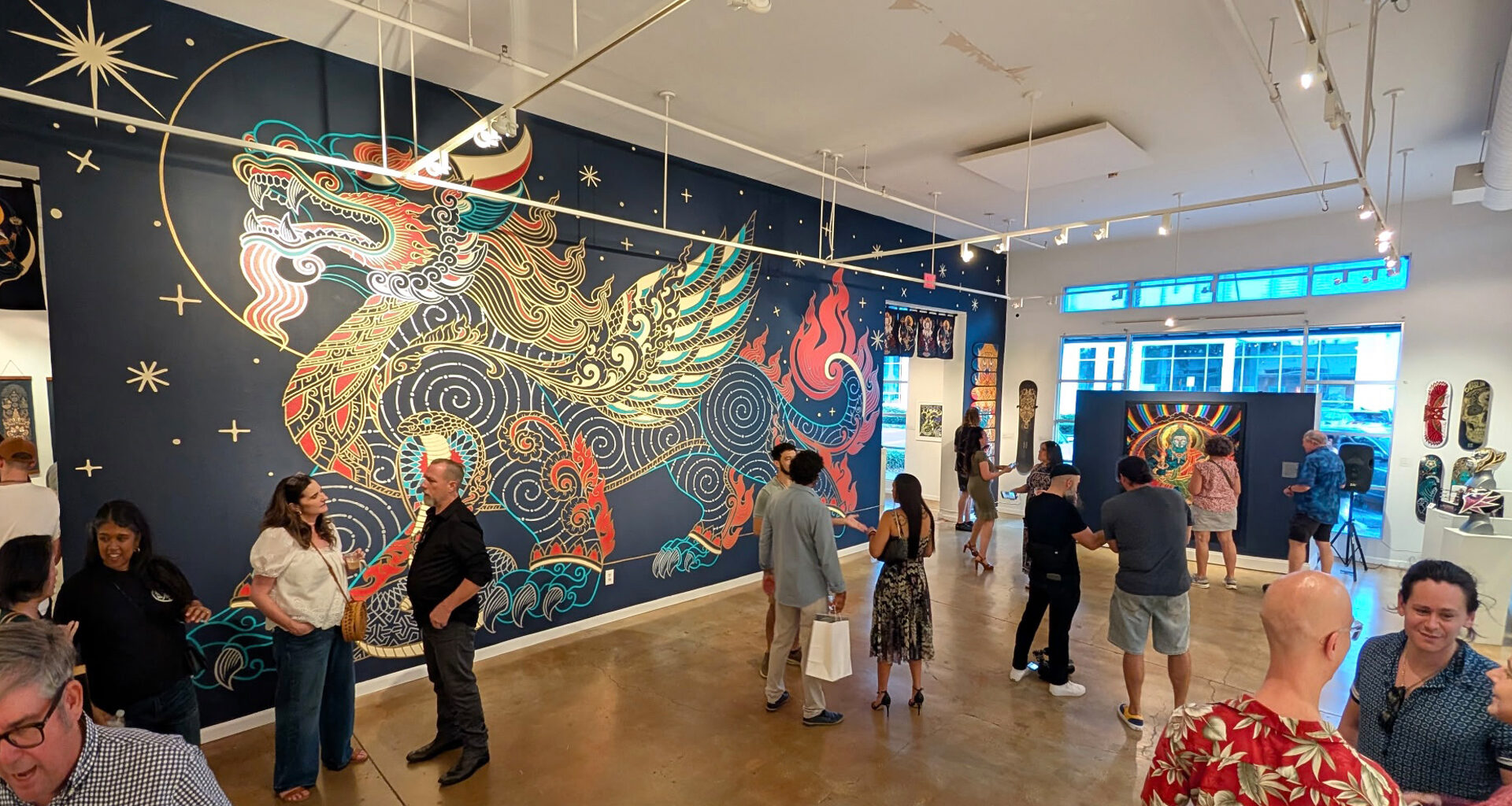 Visitors view a large, colorful dragon mural on a dark blue wall inside an art gallery.