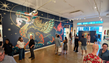 Visitors view a large, colorful dragon mural on a dark blue wall inside an art gallery.