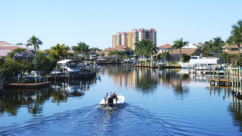A boat cruising down a canal alongside private jetties and boats belonging to canalside homes in Cape Coral