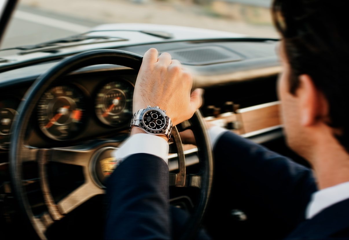 Driver wearing a chronograph watch at the wheel of a classic Porsche at Time To Drive festival