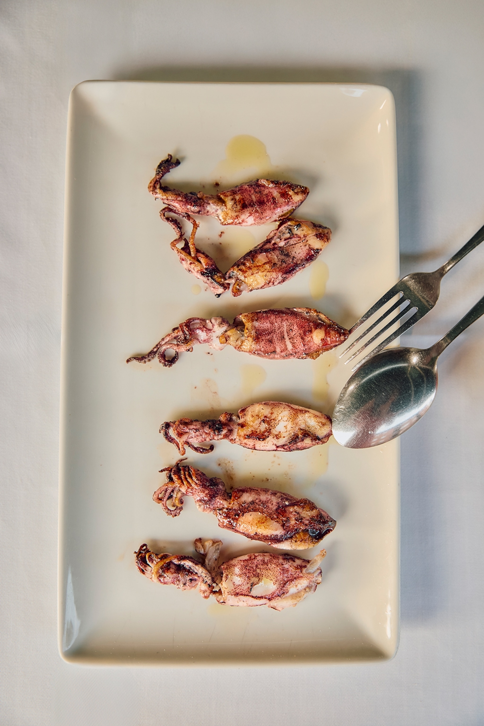 A plate of char-grilled squid neatly lined up on a rectangular plate.