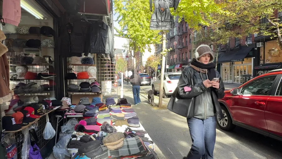 A woman walks past a hat and scarf vendor on Orchard Street on a brisk November day in 2025. (Credit: PIX11)