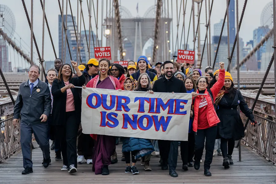 a group of people cheering holding a sign reading OUR TIME IS NOW