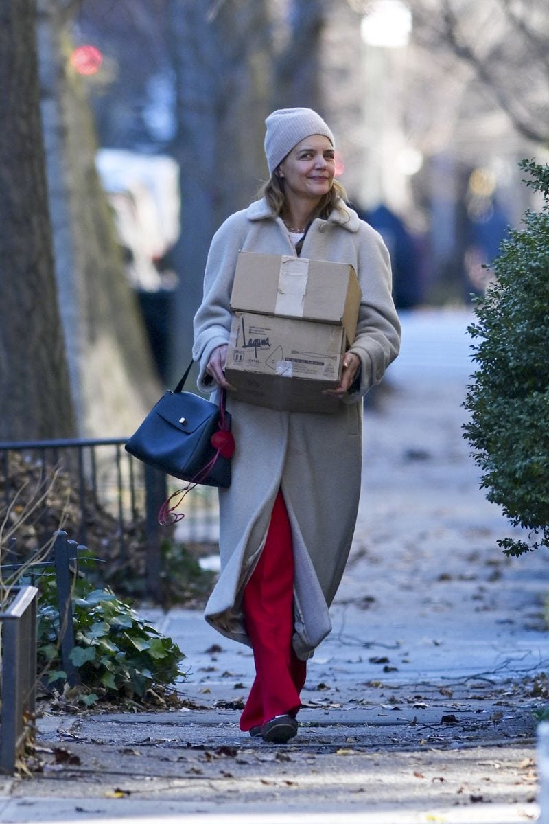 Katie Holmes wore a long light-colored coat layered over a knit beanie and wide-leg pants while carrying shopping boxes and a shoulder bag. 