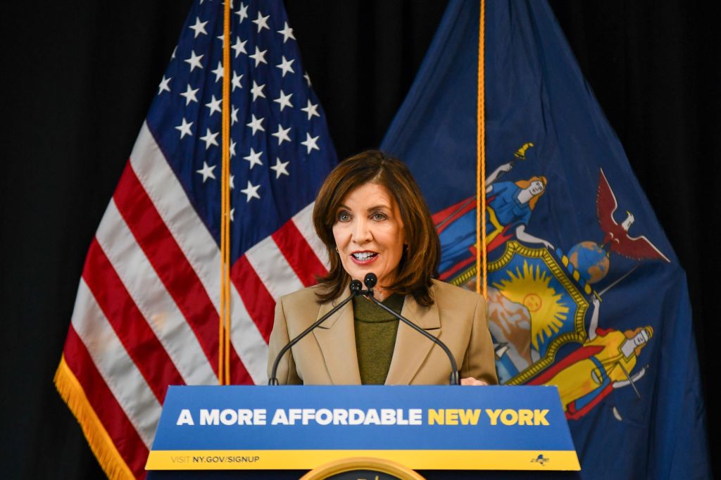 Kathy Hochul speaks at a podium in front of American and New York flags.
