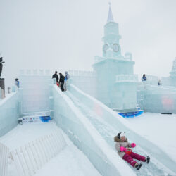 A girl slides down an ice slide built in the shape of the Kremlin for the Icy Moscow festival at the Victory park in Moscow, Russia, Tuesday, Dec. 30, 2025, as the monument to the Heroes of the First World War is seen in the background. (AP Photo/Pavel Bednyakov)