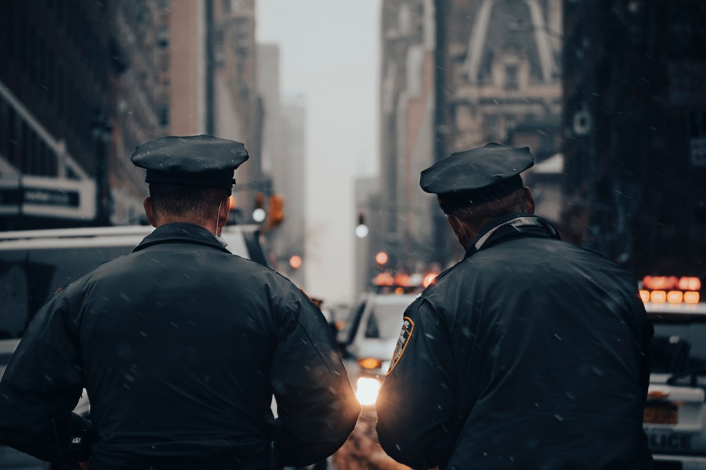 Two NYPD officers in uniform facing away from the camera in a snowy New York City street.