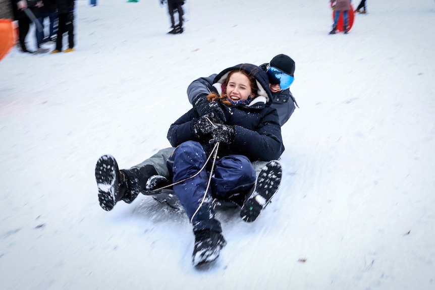 Two people ride a toboggan in the snow.