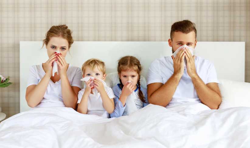Mom, Dad, and two children sitting in bed with runny nose and fever as record-breaking Flu hits New York