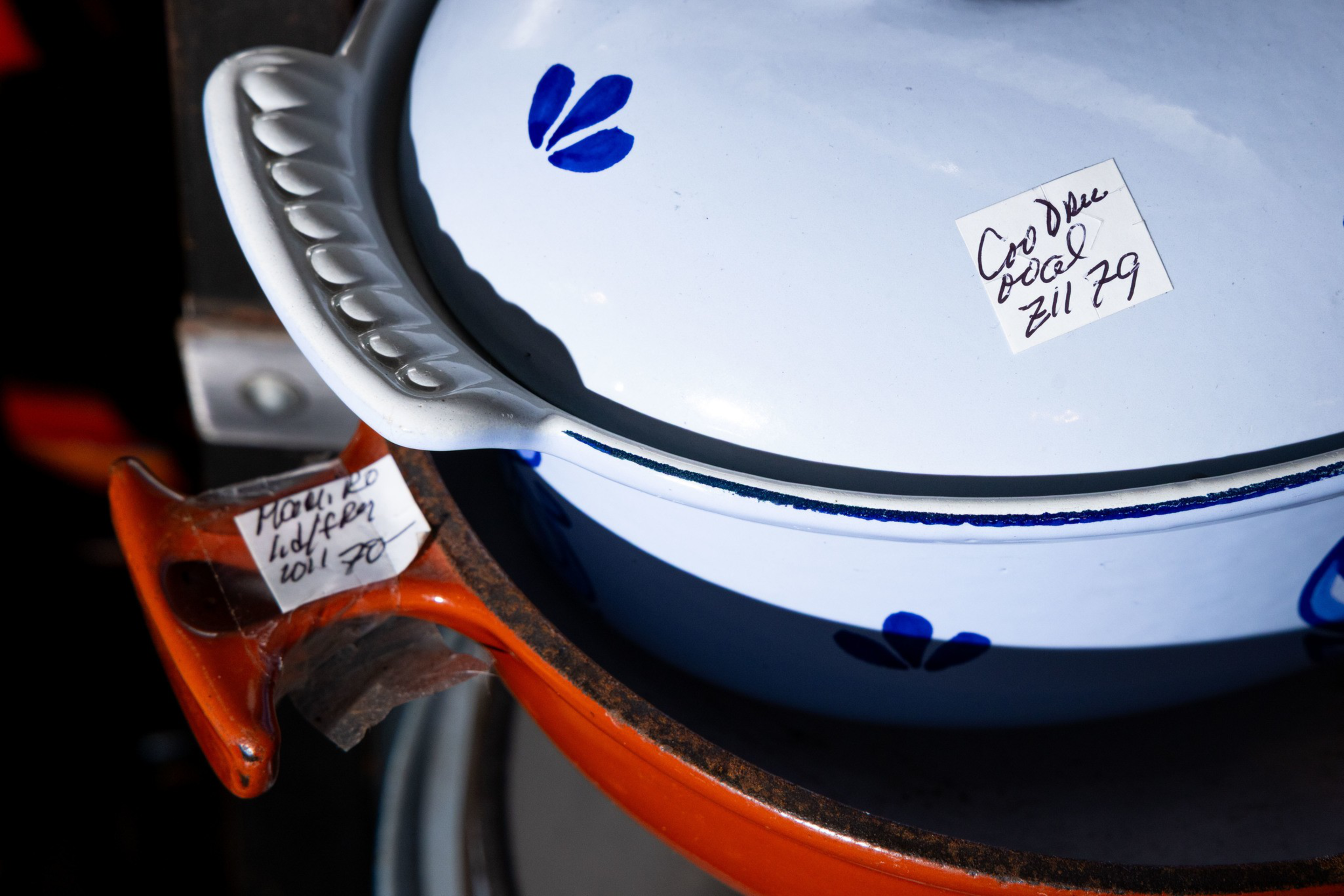 A white ceramic pot with blue flower designs sits inside a larger orange pot, both labeled with handwritten price tags.