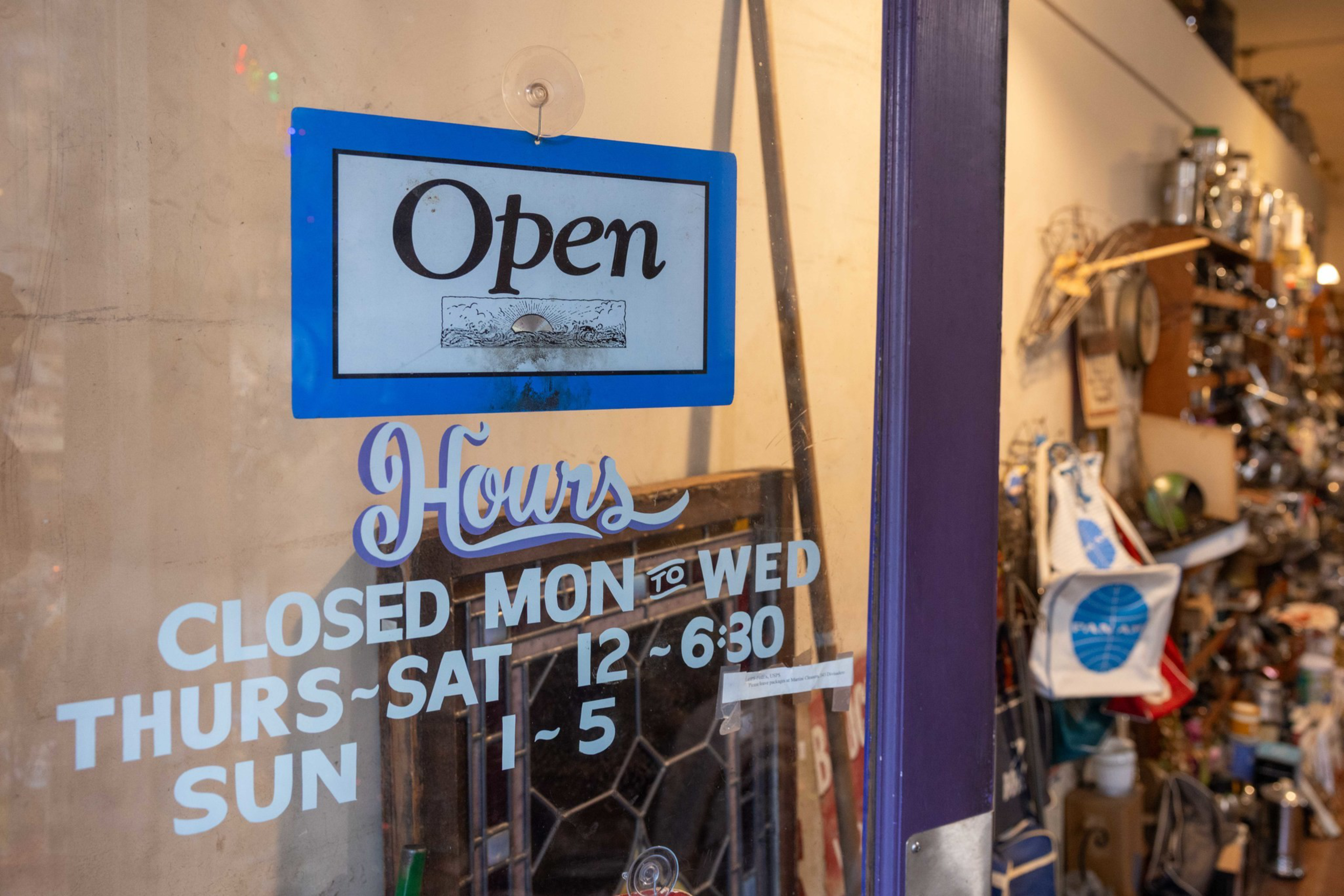 Open sign hangs on a glass door with hours showing closed Monday to Wednesday, open Thursday to Saturday 12-6:30, and Sunday 1-5.