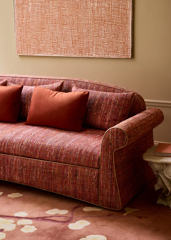 Red patterned sofa with orange cushions in a cozy living room with abstract art hanging on the wall.