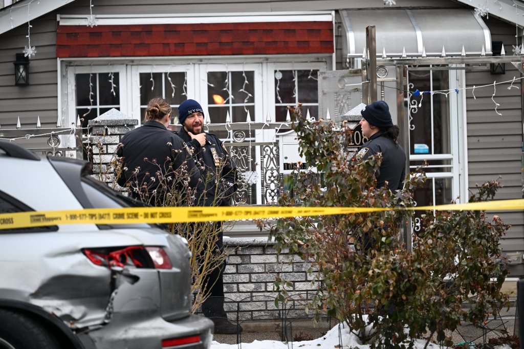 Police officers standing outside a residence cordoned off by crime scene tape.