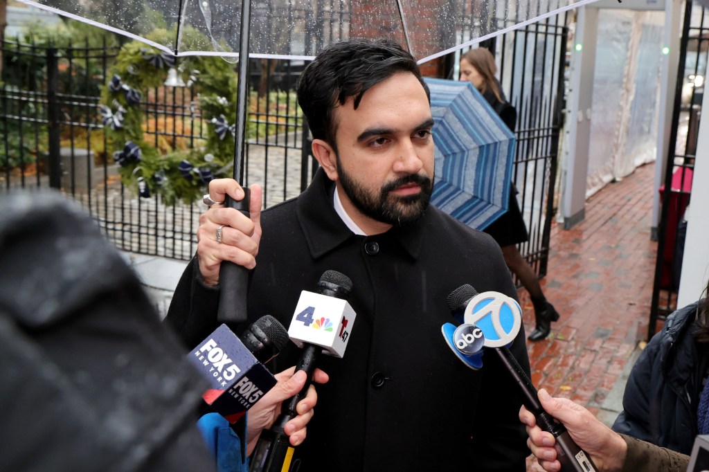 Zohran Mamdani speaks to reporters while holding an umbrella in the rain.