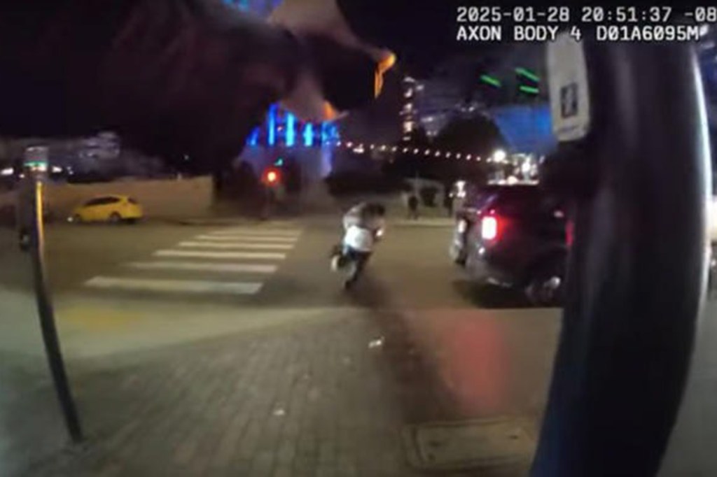 A person is crossing a street with a car behind them as seen from a body camera at night.