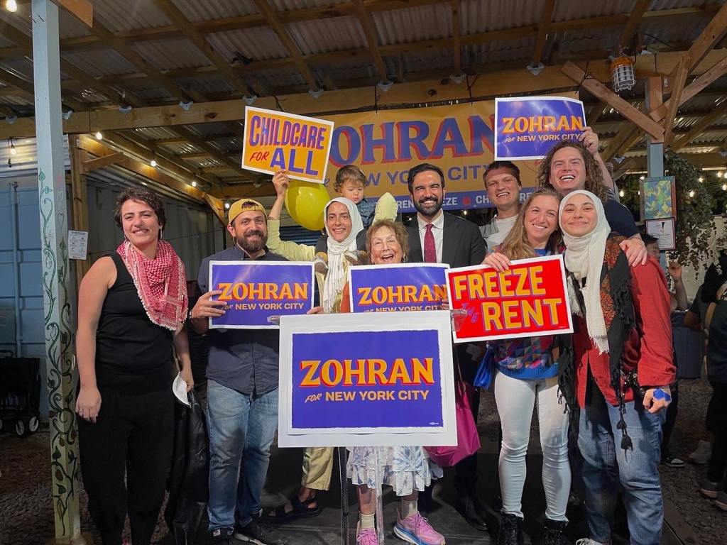 Aber Kawas, far right, with Zohran Mamdani, center, and supporters holding "Zohran for New York City," "Childcare for All," and "Freeze Rent" signs.