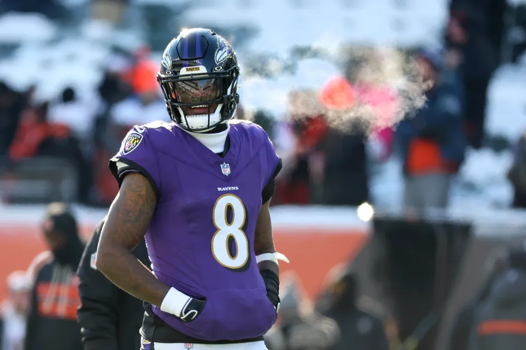 Baltimore Ravens player Lamar Jackson in a purple uniform with the number 8 on it, standing on the field with breath visible in the cold air.