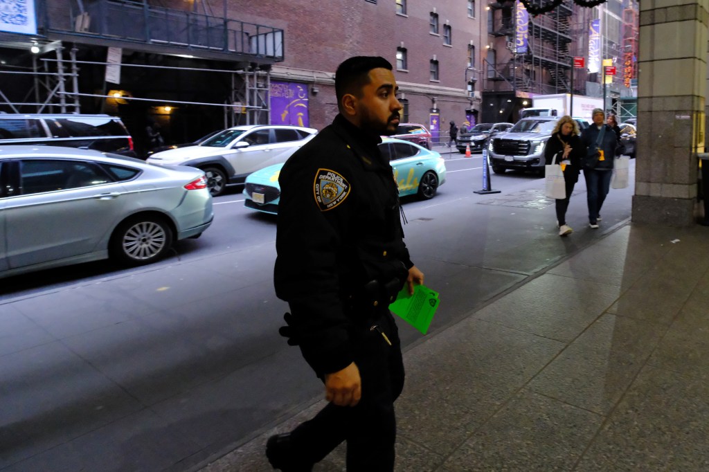 An NYPD Midtown South precinct officer walks into the Times Square Hampton Inn carrying a green sealing evidence sticker.
