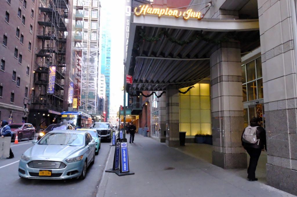 Partial view of the Times Square Hampton Inn at 220 W. 41st St., with a "Hampton Inn" sign and two "Loading Zone" signs visible.