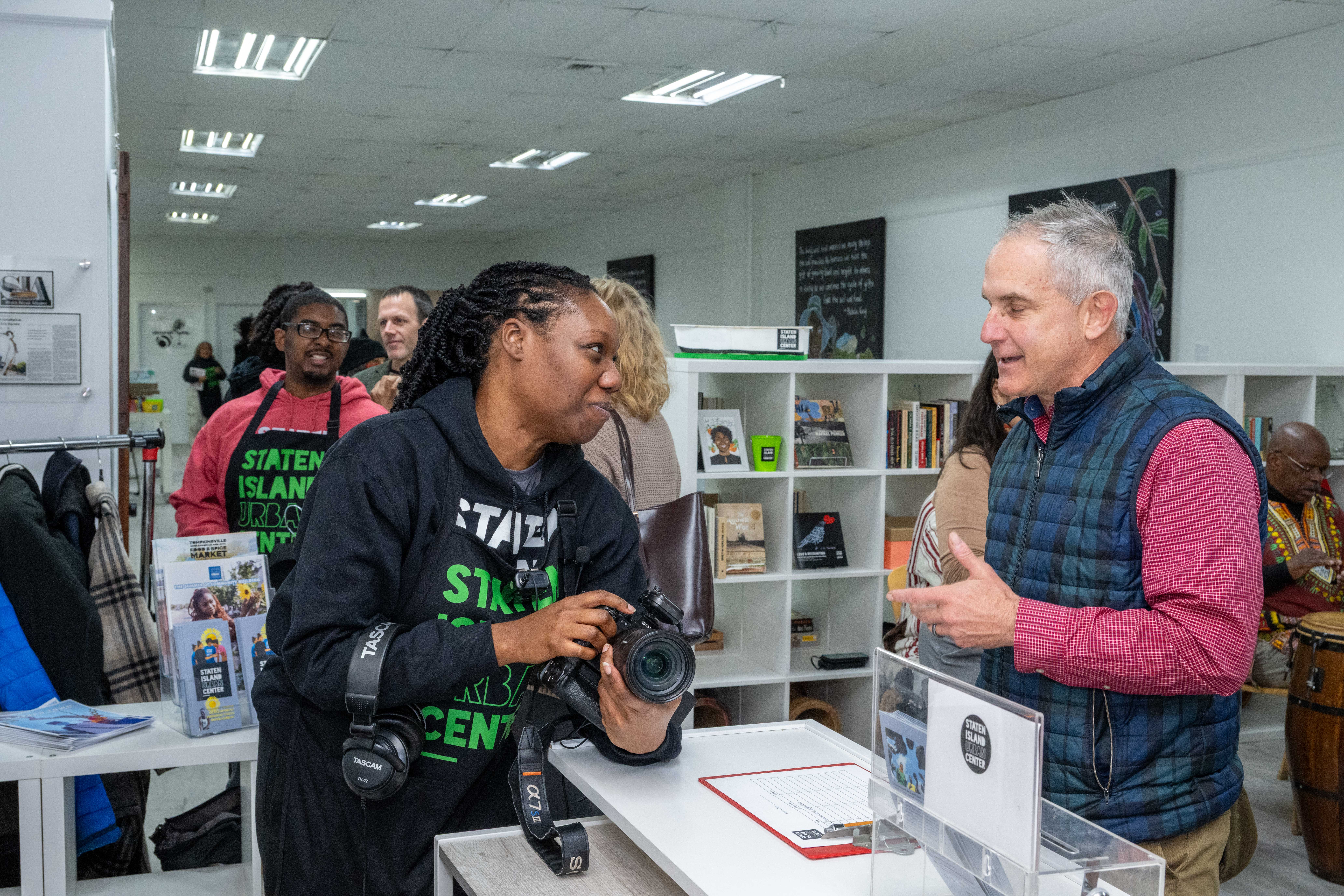 Shani Mitchell, holding a camera, welcomes guests to the grand opening of the Staten Island Urban Center’s new storefront at 206 Bay Street in Tompkinsville on Saturday, December 6, 2025. (Owen Reiter for the Advance/SILive.com)