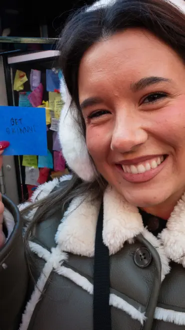 Sawyer Brooks holding a blue Post-it note with "GET SKINNY!" written on it at the Times Square Wishing Wall.
