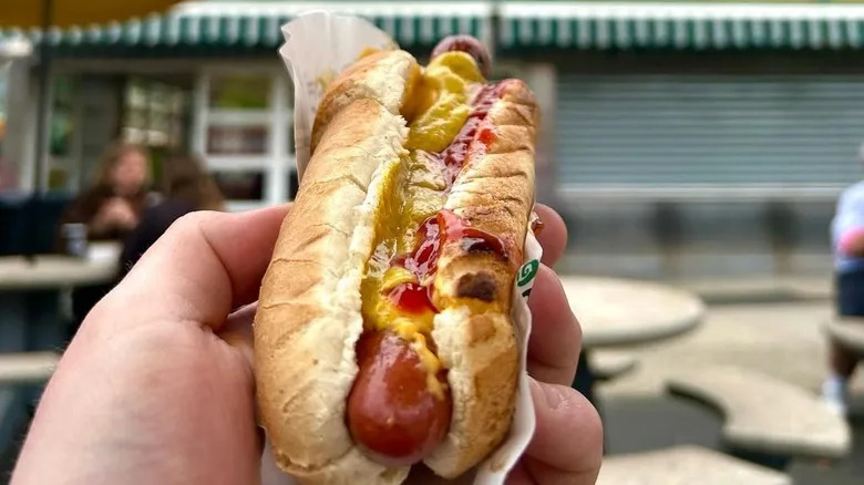 A person holds up a hot dog in front of Nathan's Famous