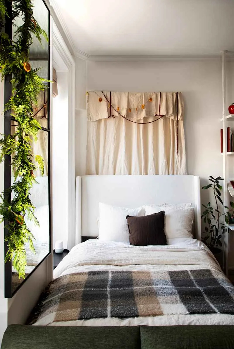 Cozy bedroom featuring a white bed with layered bedding, a plaid throw, and greenery decor.