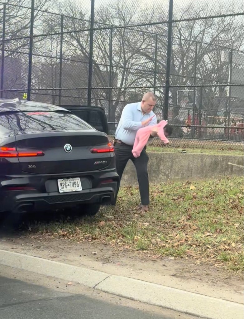 Detective Michael Greaney holds a choking baby in a pink onesie next to a black BMW on the side of a highway.