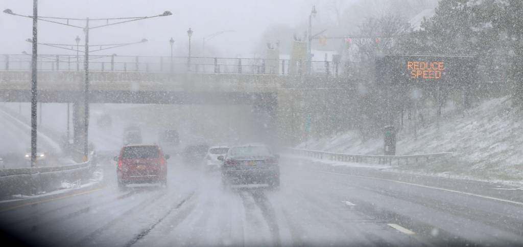 Traffic on Route 490 heading past downtown Rochester during a snowstorm with a "REDUCE SPEED" sign visible.